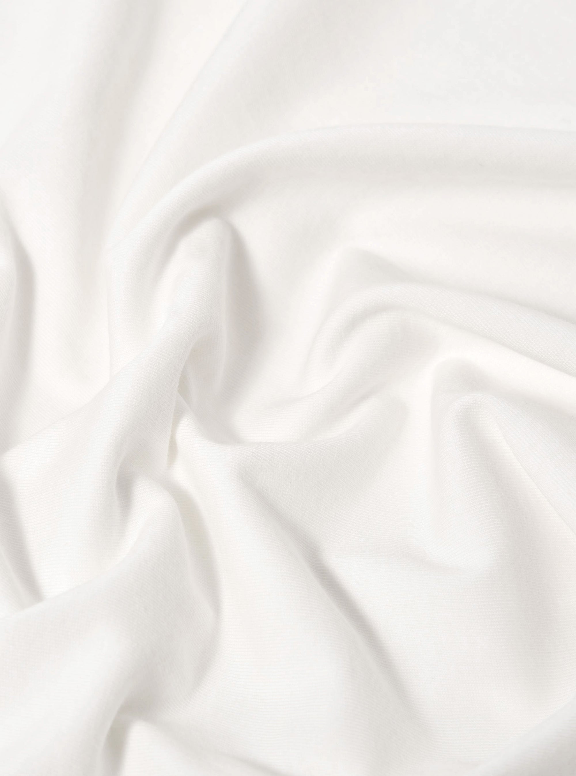 A close-up fabric swatch of the Ecru Single Jersey 34 Printed Core Tee highlights the off-white, ecru color and the smooth, fine-knit texture of the single jersey cotton. The material fills the entire frame, providing a detailed view of the garment's fabric.