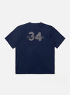 The Navy Single Jersey 34 Printed Core Tee is shown as a flat lay against a plain white background. The short-sleeve t-shirt features a ribbed crew neck and a prominent graphic print on the chest. The garment is constructed from a dark navy cotton jersey fabric with a smooth finish.