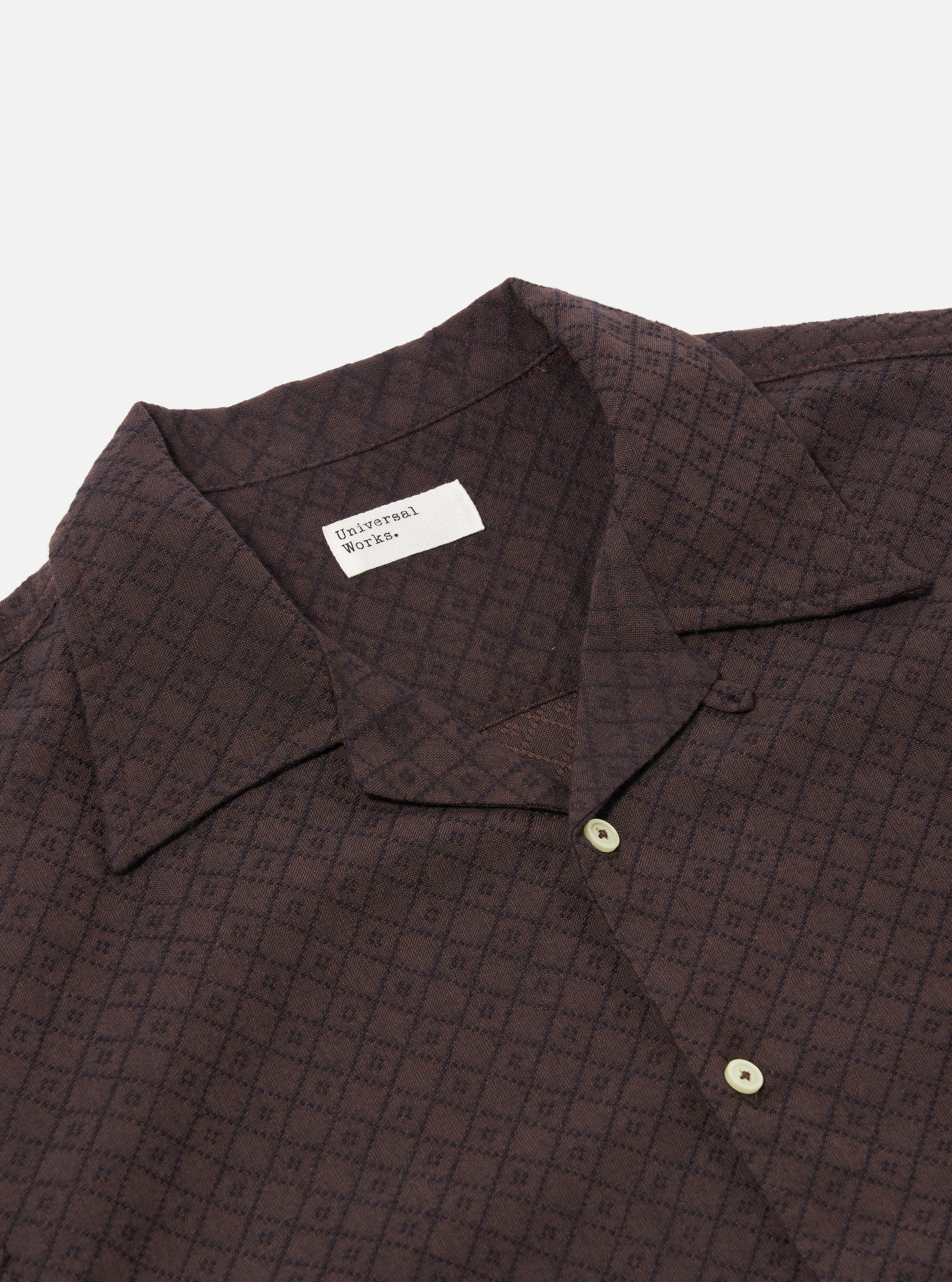 The Brown Diamond Dobby Deck Shirt is shown from the back as a flat lay against a plain white background. The image highlights the shirt's wide fit, the horizontal seam across the upper back, and the side split hem which is longer at the back than the front. The brown cotton fabric features a distinct diamond dobby texture.