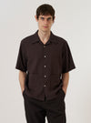 A model wears the Brown Diamond Dobby Deck Shirt against a plain, neutral background. The shirt features a brown fabric with a distinct diamond dobby texture, a classic collar, and a button-front closure. The garment is shown in a relaxed fit.