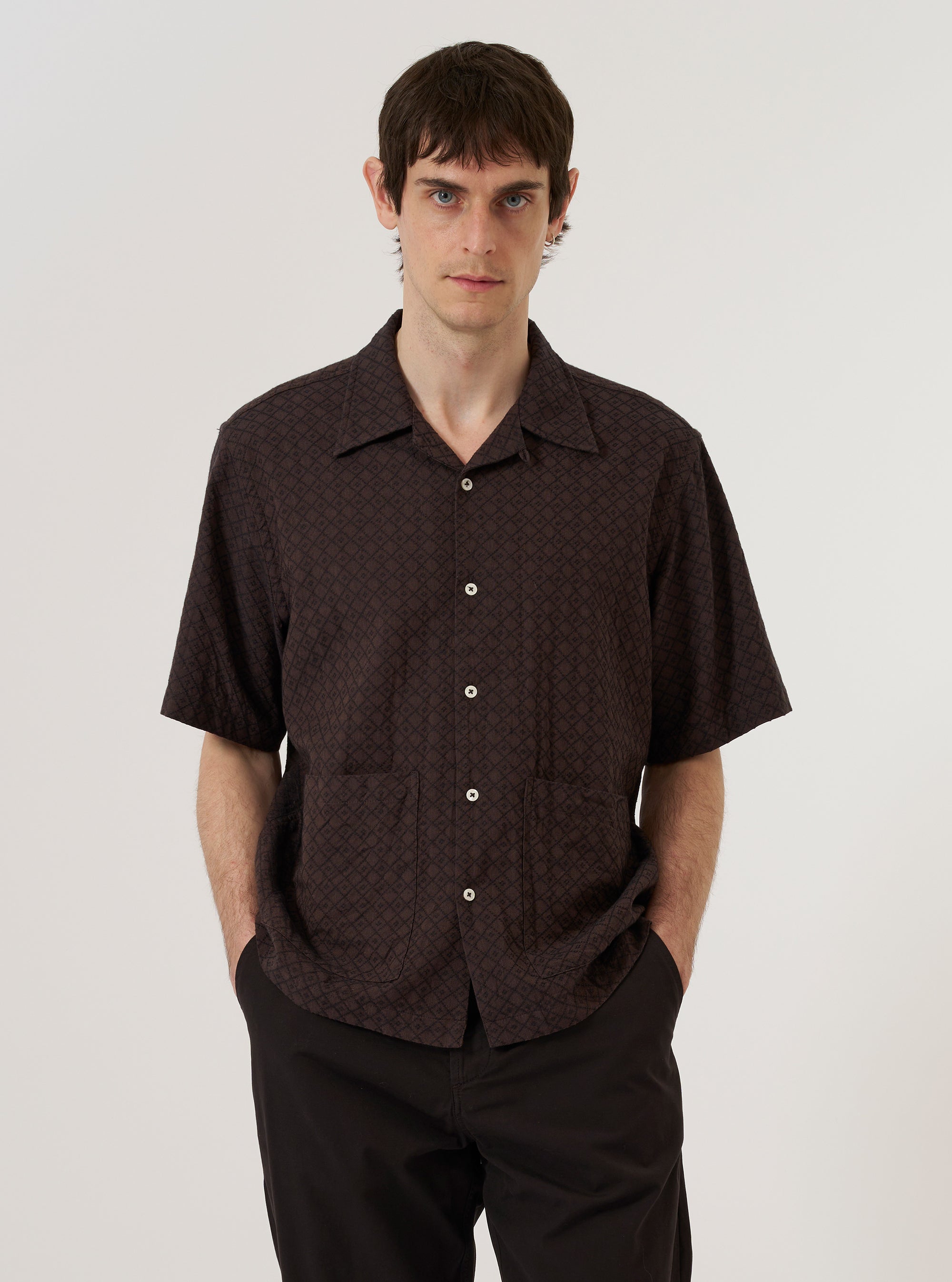 A model wears the Brown Diamond Dobby Deck Shirt against a plain, neutral background. The shirt features a brown fabric with a distinct diamond dobby texture, a classic collar, and a button-front closure. The garment is shown in a relaxed fit.