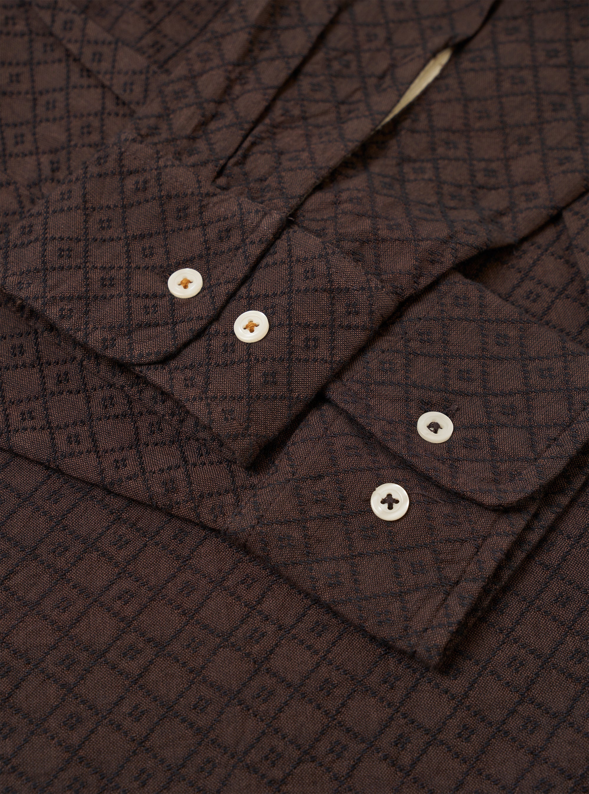 The Brown Diamond Dobby Lucky Shirt is shown from a rear angle as a flat lay against a plain white background. The image highlights the shirt's loose fit, straight hem, and the intricate diamond dobby pattern across the brown cotton fabric.