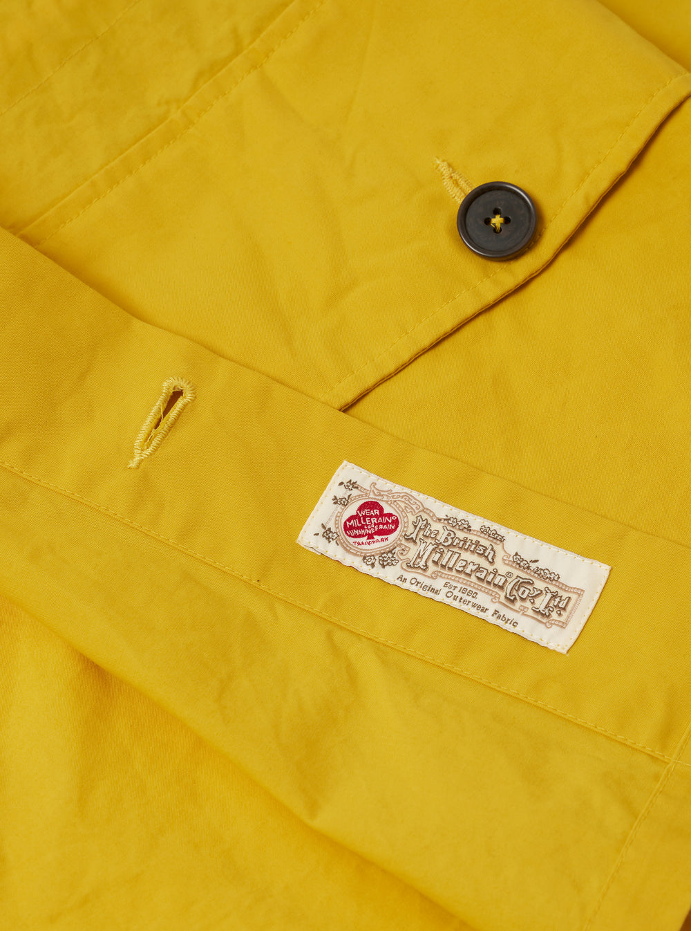 The Yellow British Wax Cotton Boston Parka is shown as a flat lay against a plain white background. The parka features an oversized silhouette with a large hood, a central button-down storm flap, one slanted chest pocket, and two prominent 3D patch pockets at the hip. The garment is constructed from a matte yellow waxed cotton fabric with visible tonal stitching and adjustable button cuffs.