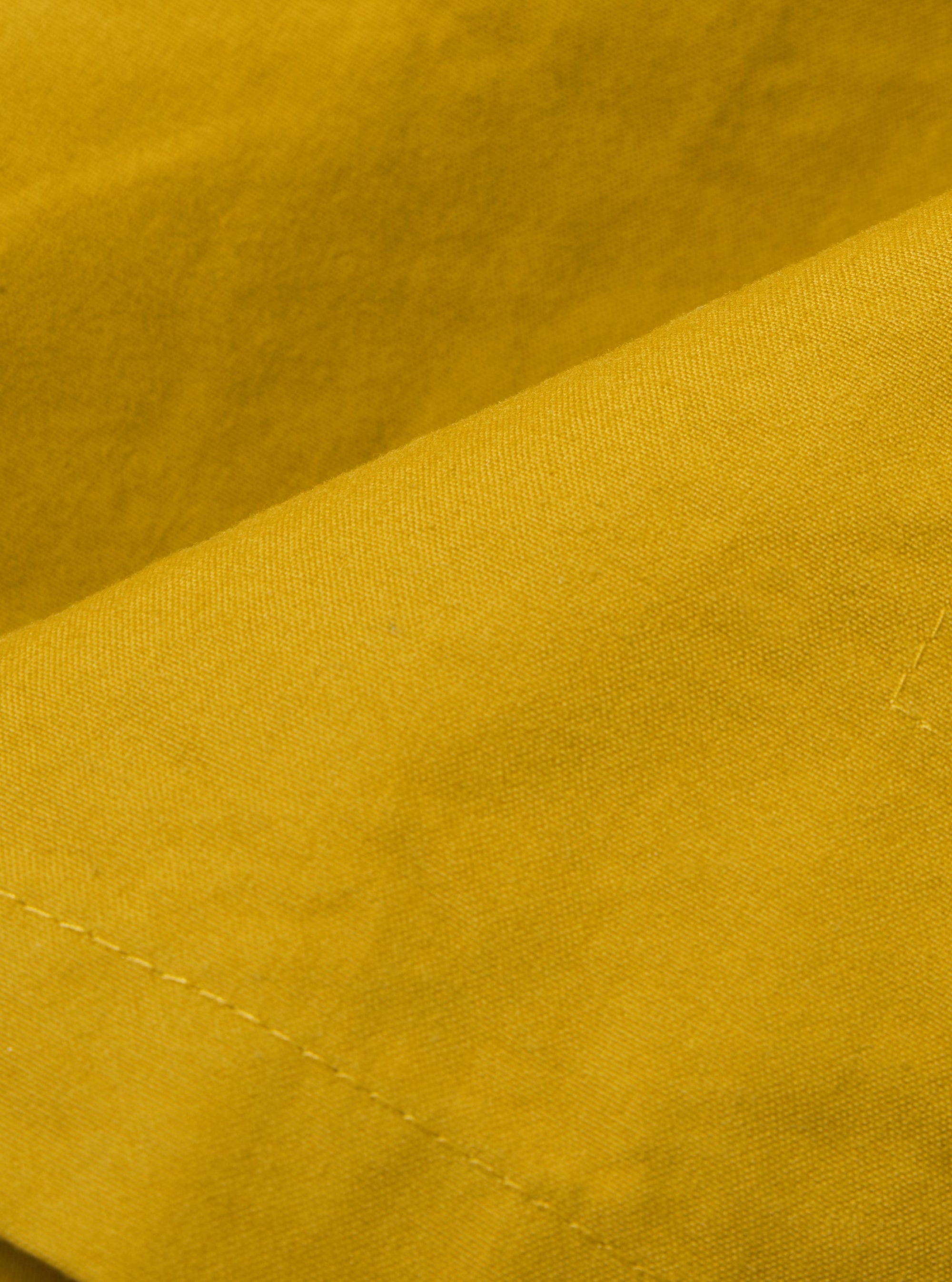 A close-up fabric swatch of the Yellow British Wax Cotton Boston Parka is shown, highlighting the vibrant yellow color and the smooth, dry texture of the British wax cotton material.