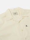 Close-up of the A. SOCIETY x Universal Works Ecru Broadcloth Camp Shirt on a white background. The shirt is ecru-colored with a camp collar and button-up front. 'A.' is embroidered on the pocket.