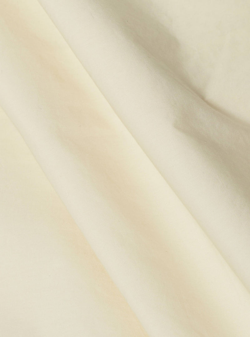 Close-up of the A. SOCIETY x Universal Works Ecru Broadcloth Camp Shirt. The ecru fabric is softly draped, showing the material's texture. Shot against a plain backdrop.