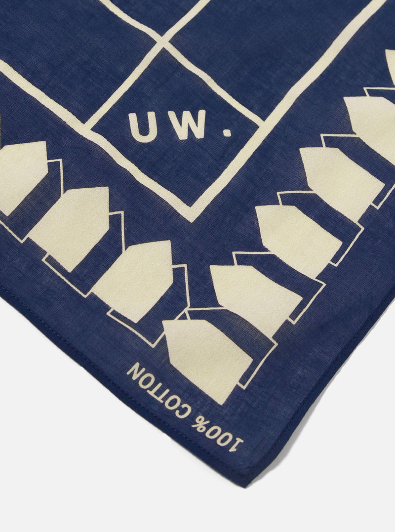 Close-up of the A. SOCIETY x Universal Works Navy Cambric Neckerchief. The navy blue cotton neckerchief has a cream-colored geometric pattern and the letters "UW." on a white background.