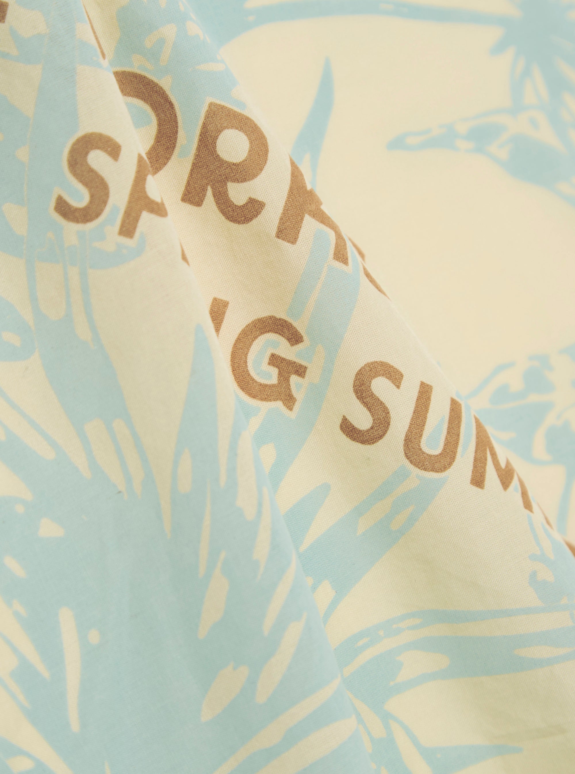 A close-up swatch image of the Cream Cambric Neckerchief fabric displays a light cream color with a smooth, fine-weave texture characteristic of cambric cotton. The material fills the entire frame, providing a detailed view of the garment's clean color and lightweight construction.