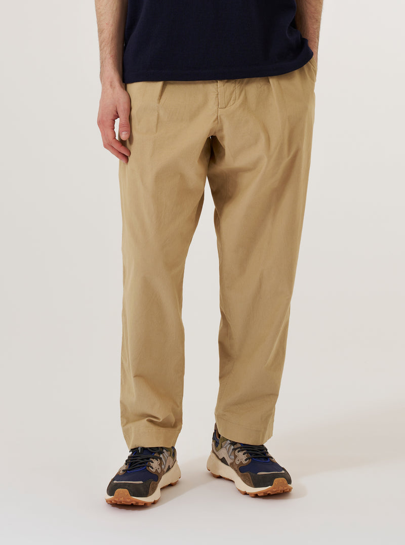 A model wears the Sand Organic Fine Cord Oxford Pant against a plain, neutral background. The trousers feature a wide, loose fit with a single pleat at the front and an elasticated waistband with a visible drawstring. The sand-colored organic cotton fabric has a fine, vertical corduroy texture.