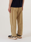 The Sand Organic Fine Cord Oxford Pant is worn by a model and shown from a rear three-quarter angle against a plain white background. The image highlights the relaxed, wide-leg fit of the trousers and the fine-ribbed texture of the sand-colored organic cotton corduroy. One rear pocket with a buttoned flap is visible. The model is wearing the pants with white socks and dark shoes.