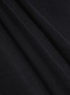 A close-up fabric swatch of the Black Organic Fine Cord Oxford Pant displays the black color and the fine, ribbed texture of the organic cotton corduroy material. The fabric fills the frame, highlighting its detailed construction.