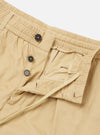 The Sand Organic Fine Cord Oxford Pant is shown in a detail view as a flat lay against a plain white background. The image focuses on the rear construction of the trousers, highlighting a buttoned flap pocket on the left and a buttoned jetted pocket on the right. The fine corduroy texture of the sand-colored organic cotton fabric and the elasticated portion of the waistband are clearly visible.