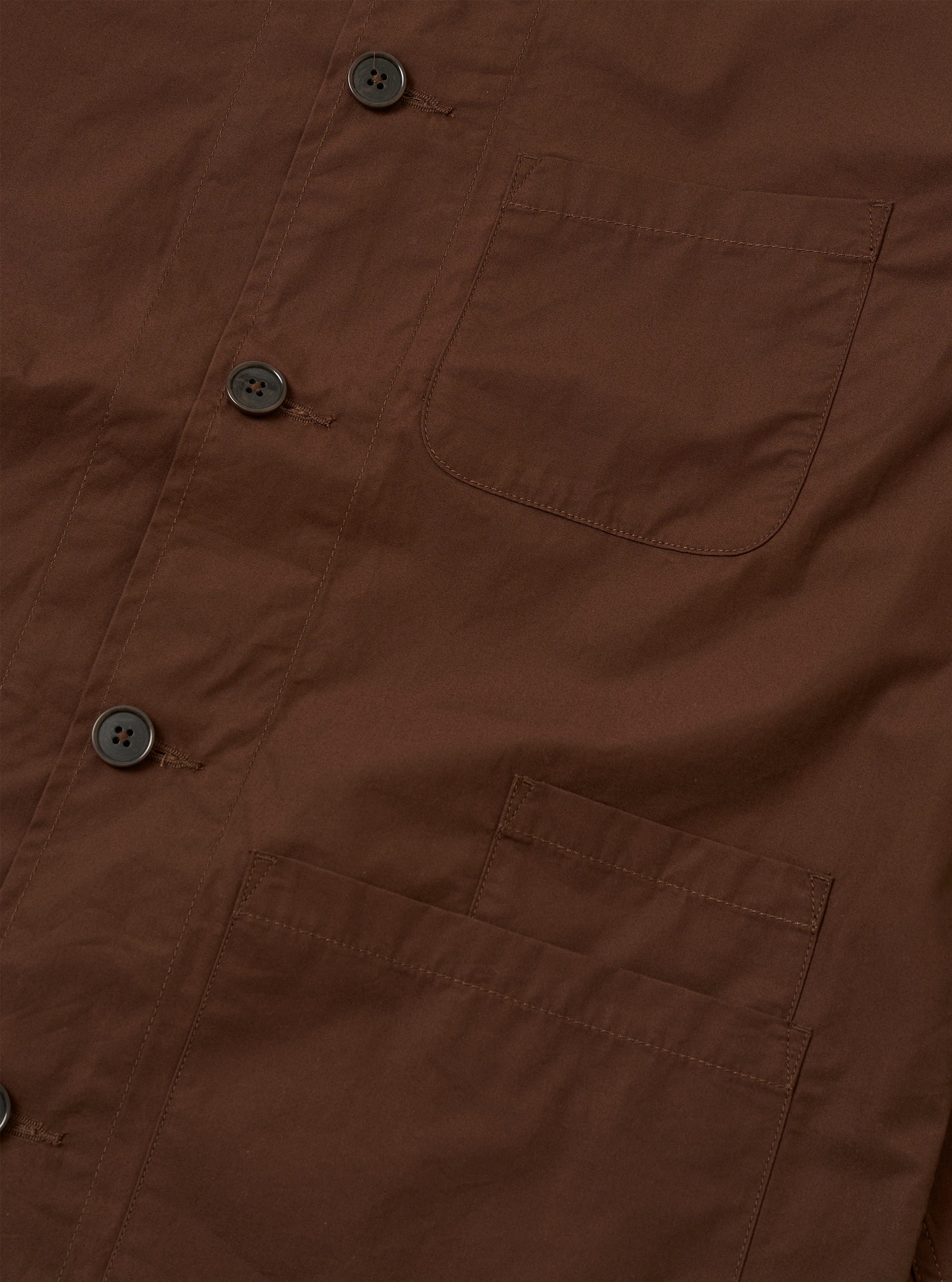 The Brown Peached Poplin Bakers Overshirt is shown from the back as a flat lay against a plain white background. The image highlights the clean construction of the garment's rear panel, featuring a straight hem and a simple, smooth finish on the brown cotton poplin fabric.