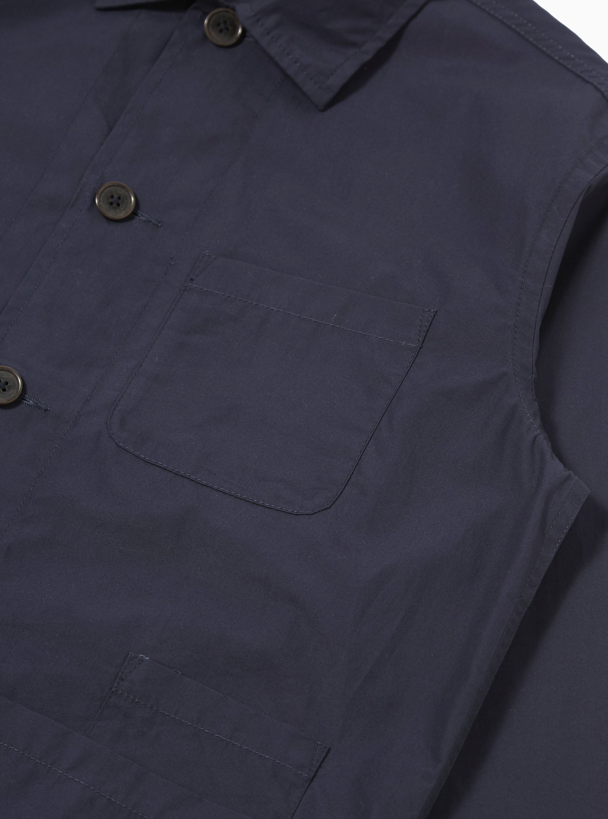 The Navy Peached Poplin Bakers Overshirt is shown from the back as a flat lay against a plain white background. The image highlights the clean, straight-cut hem, the one-piece collar, and the smooth texture of the navy blue peached cotton poplin fabric.