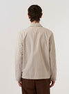 A model is wearing the Brown Kennedy Stripe Franck Jacket, shown from the back against a plain white background. The jacket features a vertical stripe pattern in shades of brown and a shorter, chore-style cut with a straight hem. The model is standing with their back to the camera, highlighting the clean construction of the garment's rear panel and the flat collar.