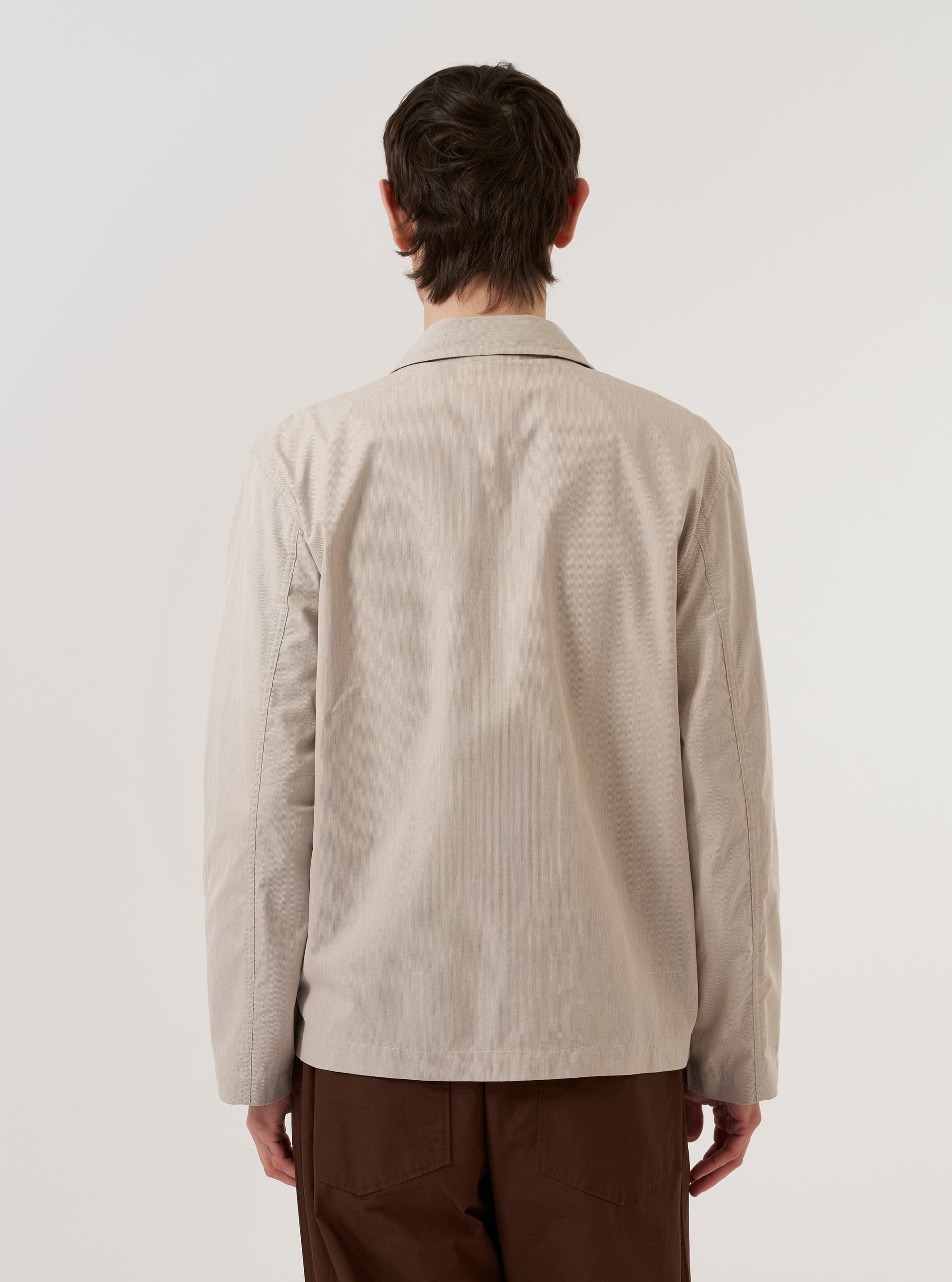 A model is wearing the Brown Kennedy Stripe Franck Jacket, shown from the back against a plain white background. The jacket features a vertical stripe pattern in shades of brown and a shorter, chore-style cut with a straight hem. The model is standing with their back to the camera, highlighting the clean construction of the garment's rear panel and the flat collar.