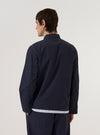 A model wears the Navy Peached Poplin Franck Jacket against a plain, light-colored background. The jacket features a classic collar, a tonal button-down front, and large patch pockets at the waist. The smooth, matte texture of the navy peached poplin fabric is visible. The model is shown from a front-facing perspective to highlight the garment's clean lines and fit.