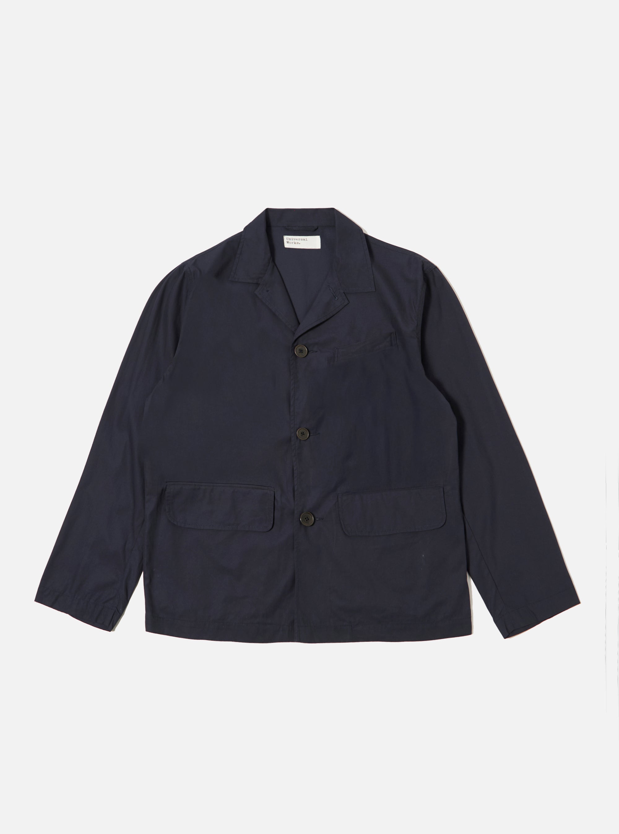 The Navy Peached Poplin Franck Jacket is shown as a flat lay against a plain white background. This short-cut chore jacket features a one-piece flat collar, a central button-down closure, two front flap pockets at the waist, and a single welt pocket on the chest. The navy blue cotton fabric has a smooth, peached poplin finish.