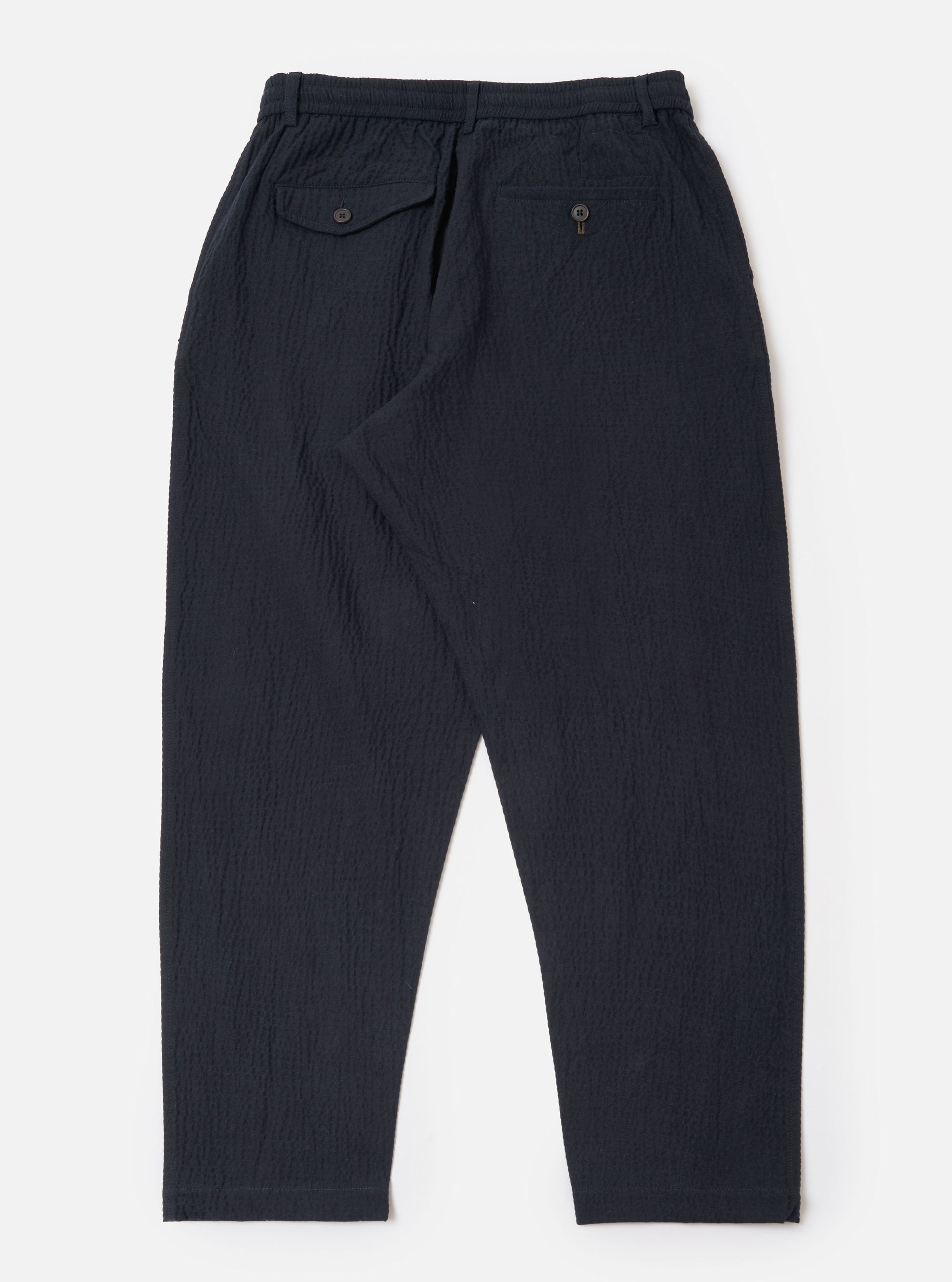 The Dark Navy Ospina Cotton Pleated Track Pant is shown from the rear as a flat lay against a plain white background. The image highlights the elasticated waistband and the rear patch pockets. The dark navy fabric features a visible puckered seersucker texture.