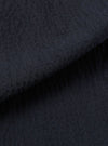 A close-up swatch of the Dark Navy Ospina Cotton Pleated Track Pant highlights the fabric's deep navy color and puckered seersucker texture. The material fills the frame, providing a detailed view of the recycled cotton blend's weave.
