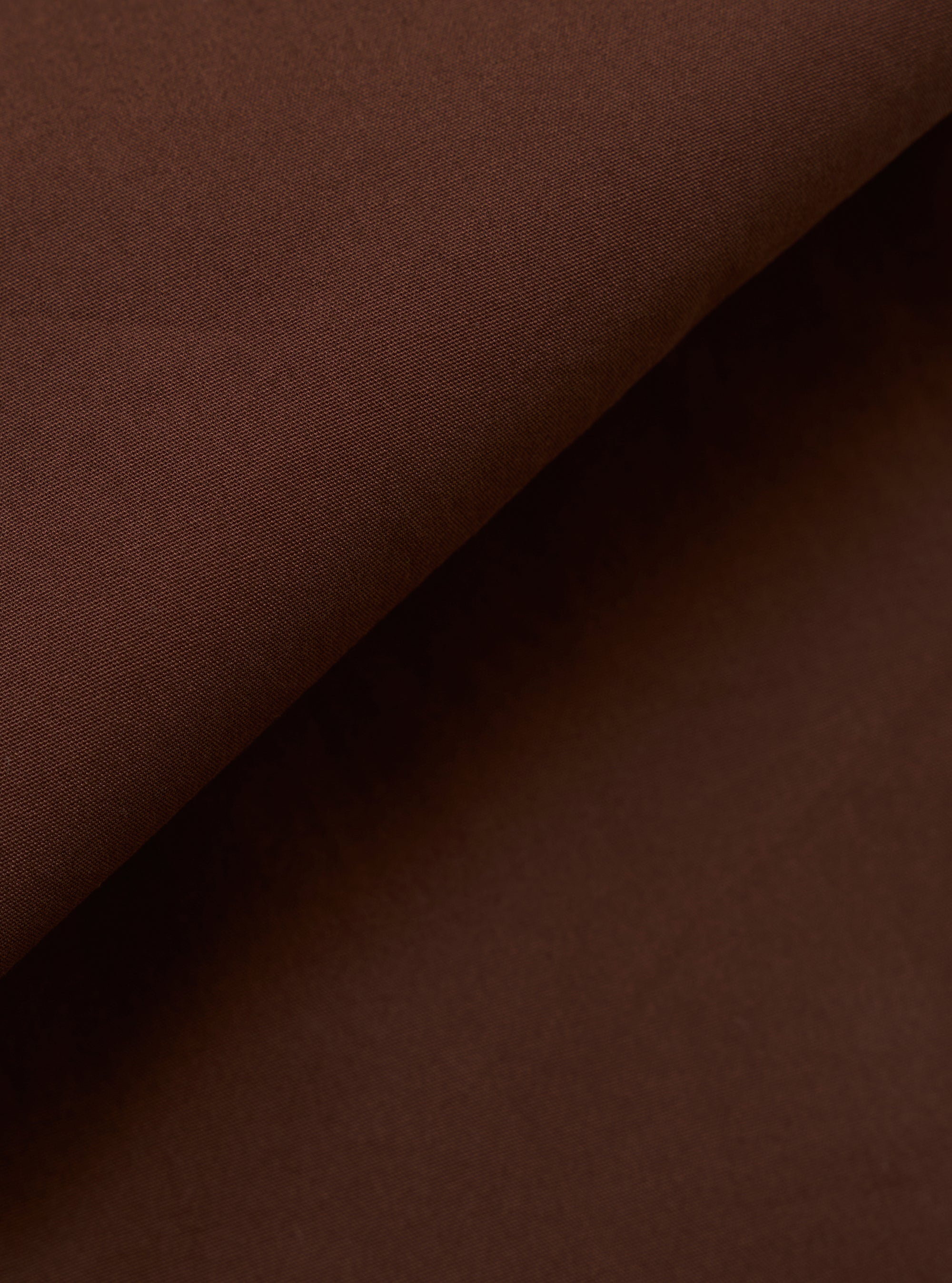 A close-up swatch image of the Brown Peached Poplin Military Chino fabric highlights the solid brown color and the smooth, matte finish of the peached poplin material. The textile's fine weave is clearly visible.