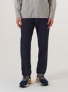 A model wears the Navy Peached Poplin Military Chino against a plain white background. The image shows a front view of the trousers, highlighting the straight-leg fit, button waist closure, and side pockets. The dark navy cotton fabric has a smooth, peached finish. The model is shown from the waist down, wearing the chinos with a light-colored shirt tucked in.