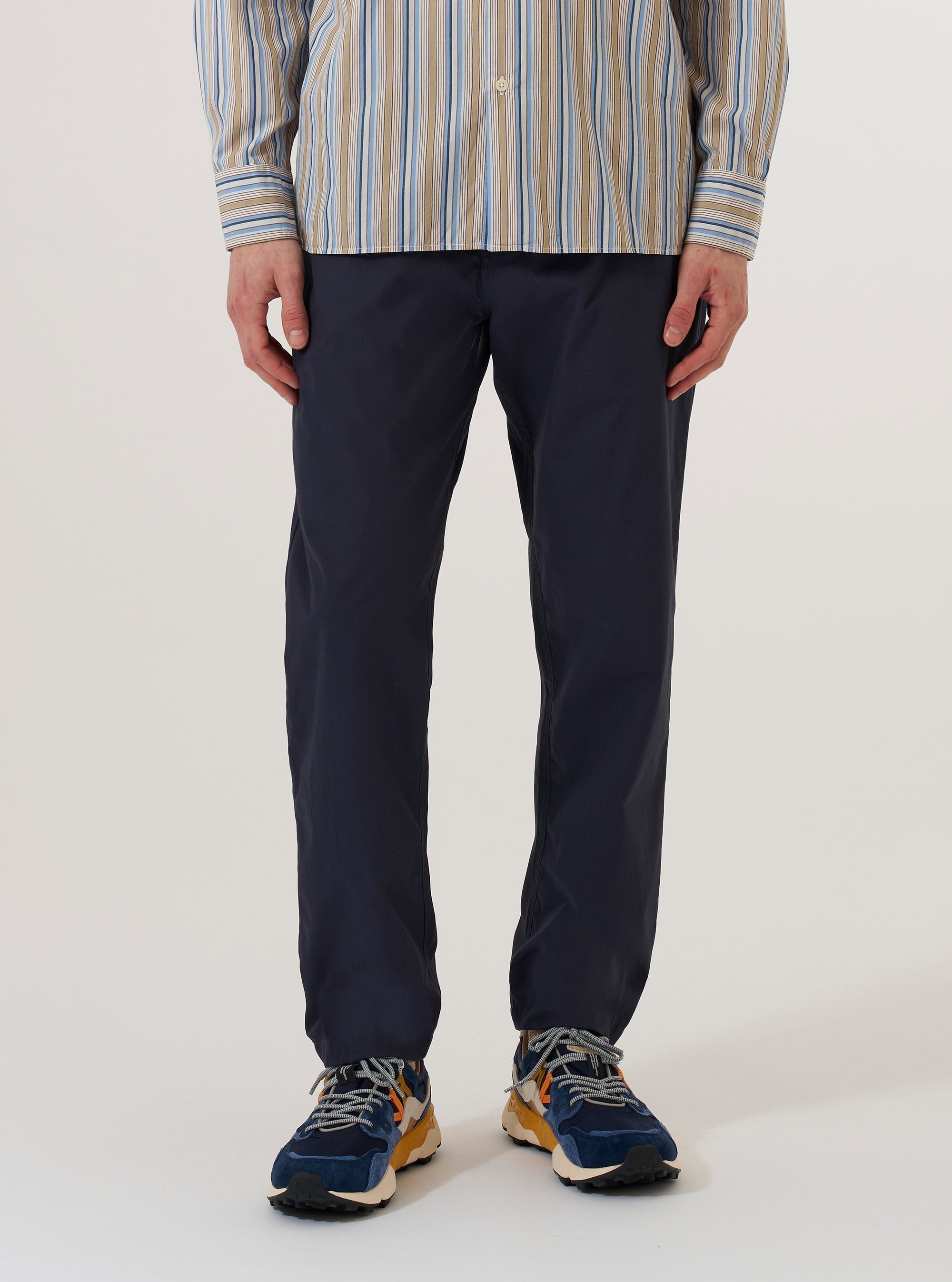 A model wears the Navy Peached Poplin Military Chino against a plain white background. The image shows a front view of the trousers, highlighting the straight-leg fit, button waist closure, and side pockets. The dark navy cotton fabric has a smooth, peached finish. The model is shown from the waist down, wearing the chinos with a light-colored shirt tucked in.