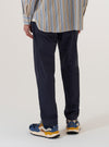 A model is wearing the Navy Peached Poplin Military Chino, shown from the waist down from a rear angle against a plain white background. The trousers feature a straight-leg silhouette and a rear flap pocket with a button closure. The navy blue fabric has a smooth, matte peached poplin finish.