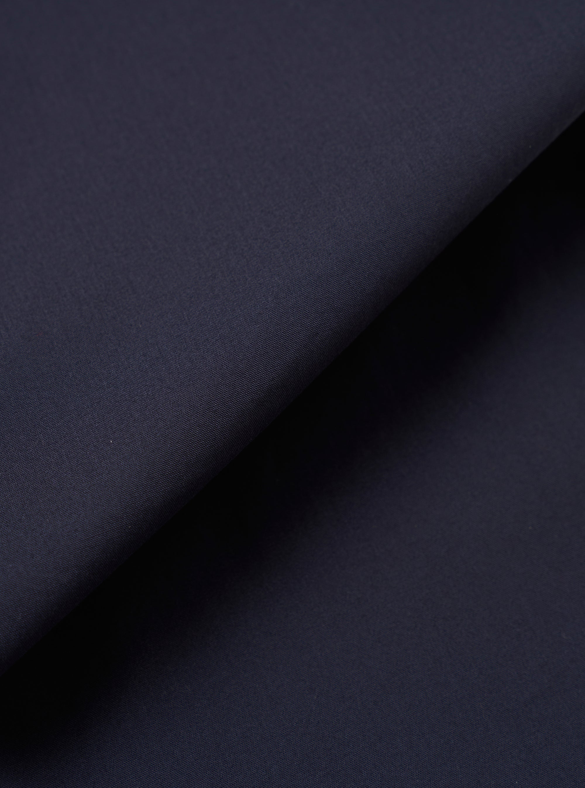A close-up swatch image of the Navy Peached Poplin Military Chino fabric highlights the deep navy blue color and the smooth, fine-grained texture of the peached cotton poplin. The material fills the frame, providing a detailed view of the garment's color and weave.