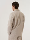 A model wears the Brown Kennedy Stripe Three Button Jacket over a light-colored top, shown from the back against a plain white background. The image highlights the jacket's rear construction, featuring a center back seam and a single vent at the hem. The brown fabric is detailed with a subtle vertical stripe pattern.