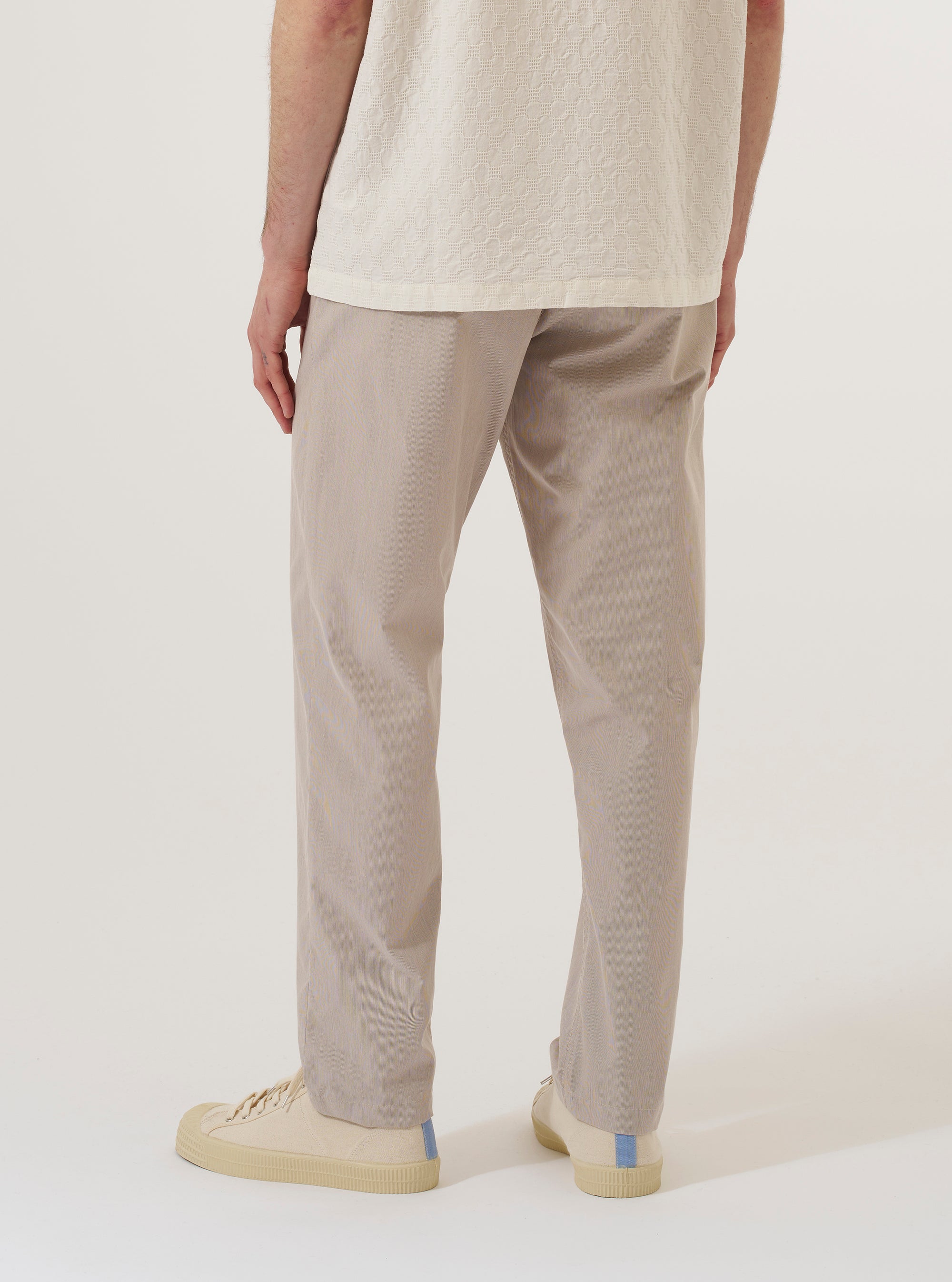 A model wears the Brown Kennedy Stripe Military Chino, shown from a rear angle against a plain white background. The trousers feature a distinct vertical stripe pattern in shades of brown and a classic straight-leg fit. The image highlights the back patch pockets and the structured construction of the military-style chinos.