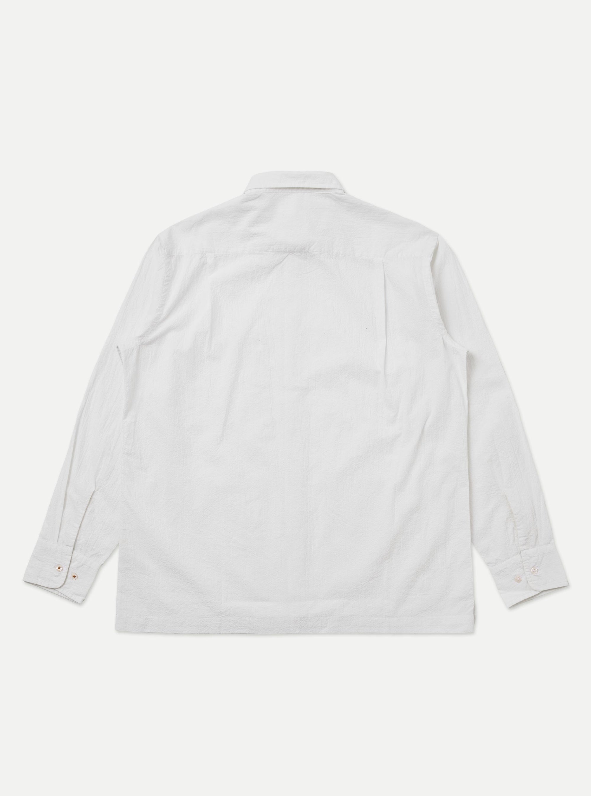 A close-up fabric swatch of the White Seersucker Double Lucky Shirt displays a crisp white color with the characteristic puckered, rippled texture of seersucker. The fine, alternating tighter and looser cotton warp threads create a series of small, raised ridges across the surface of the material. There is no model or mannequin present in the image.