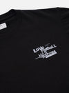 The Black Love Football Jersey Print Tee is shown from the back as a flat lay against a plain white background. The image highlights the clean construction of the rear panel, the short sleeves, and the ribbed crew neck. The garment is made from a solid black cotton jersey fabric.