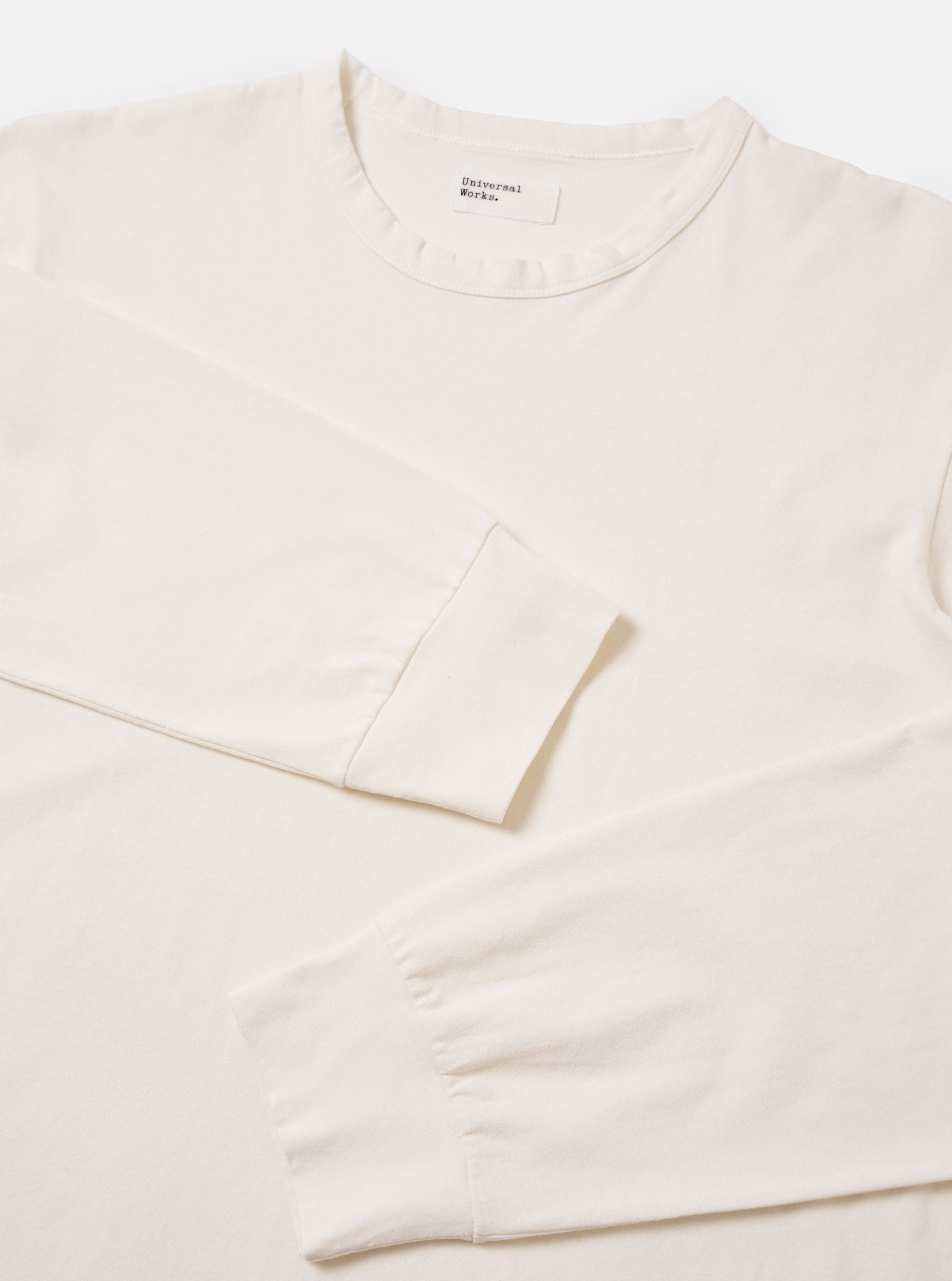The Antique White Recycled/Bio Jersey Henry L/S Tee is shown from a rear angle as a flat lay against a plain white background. The image highlights the clean construction of the shoulders, the long sleeves, and the straight hem. The jersey fabric is a solid antique white color with a soft, smooth texture.