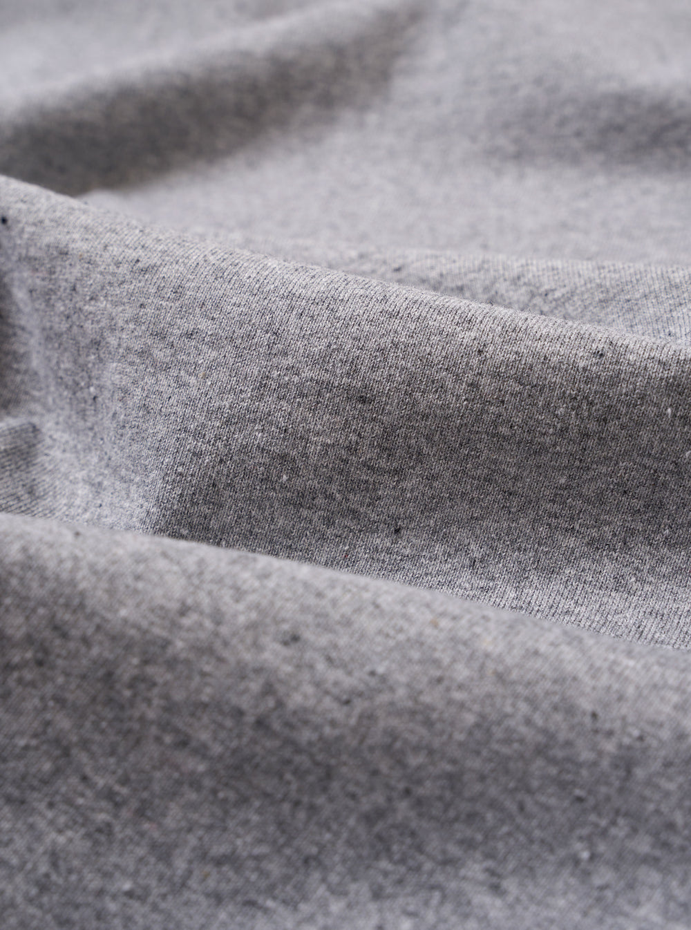 A close-up fabric swatch of the Grey Marl Recycled/Bio Jersey Henry L/S Tee highlights the speckled grey marl color and the soft, knitted texture of the recycled and organic cotton jersey fabric.