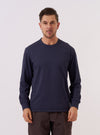 A model wears the Navy Recycled/Bio Jersey Henry L/S Tee against a plain, light-colored background. The long-sleeve t-shirt features a crew neckline, ribbed cuffs, and a relaxed fit. The navy blue jersey fabric appears soft with a matte finish. The image is a medium shot, focusing on the front and fit of the garment on the model.