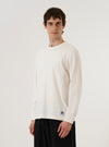 A model wears the Antique White Recycled/Bio Jersey Henry L/S Tee against a plain white background. The long-sleeved top features a three-button front placket at the neckline and is made from a smooth, off-white jersey fabric. The model is shown from the front, highlighting the garment's relaxed fit and clean construction.
