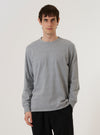 A model wears the Grey Marl Recycled/Bio Jersey Henry L/S Tee, standing against a plain, neutral studio background. The long-sleeved tee features a classic crew neckline and a relaxed fit, crafted from a light grey marl jersey fabric with a soft, heathered texture. The garment is shown worn over the model's torso, highlighting its simple, functional design.