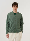 A model wears the Green Argyll Jersey Cardigan against a plain white background. The cardigan features an all-over tonal green Argyll diamond pattern, a five-button front closure, and ribbed detailing at the V-neckline, cuffs, and hem. The model is shown from the front, wearing the garment over a light-colored t-shirt.