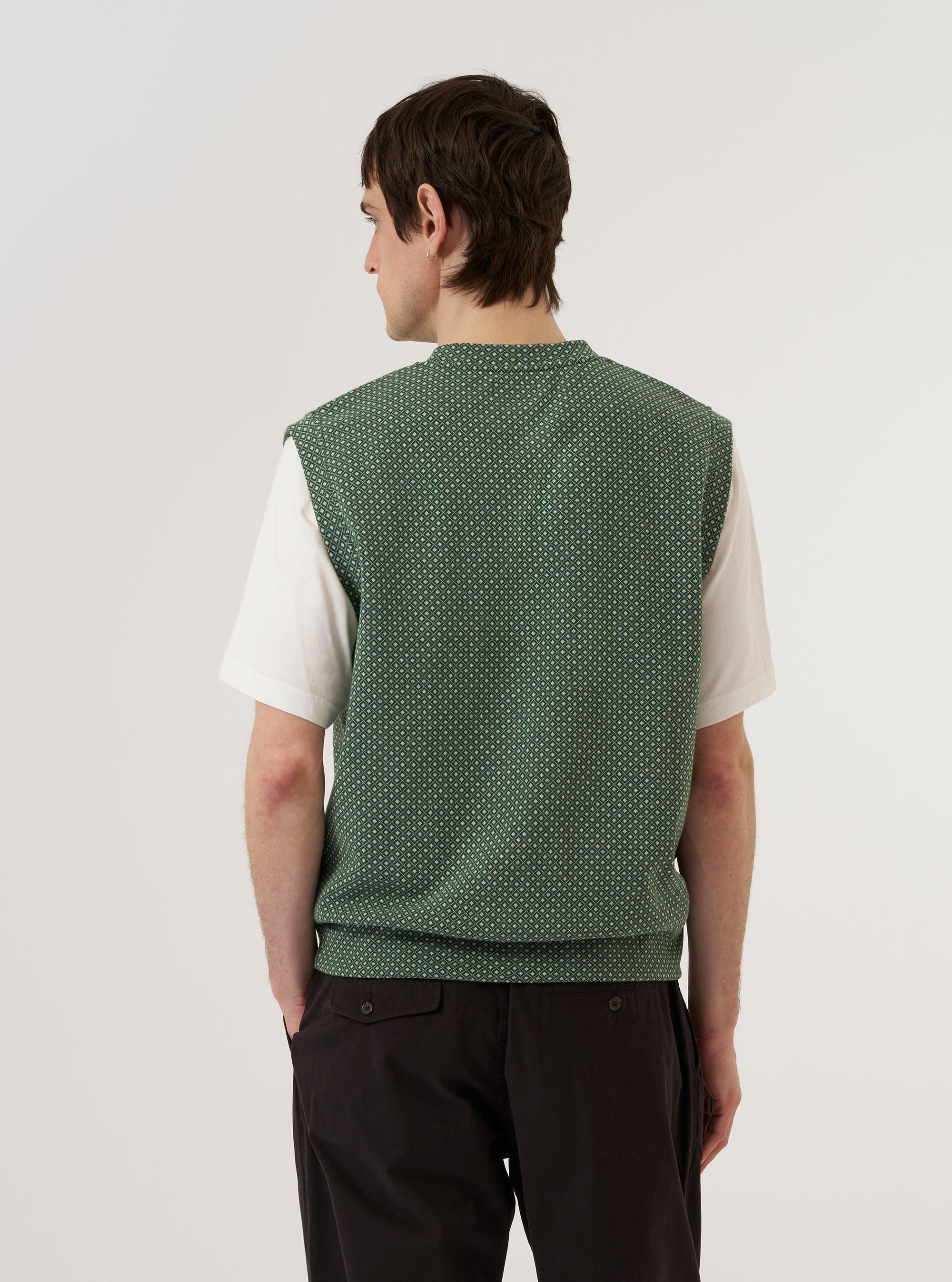 A model wears the Green Argyll Jersey Sleeveless Crew against a plain white background. The sweater vest features a green diamond argyll pattern with a ribbed crew neck and sleeveless armholes. The model is shown from the waist up, demonstrating the fit of the knit garment over the torso.