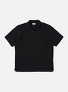 The Black Fantasy Checkerboard Vacation Polo is shown as a flat lay against a white background. The polo features an all-over black and grey checkerboard pattern, a one-piece open collar, a short buttonless placket, and a single patch pocket on the left chest. The short-sleeve garment has a stepped hem with side vents.