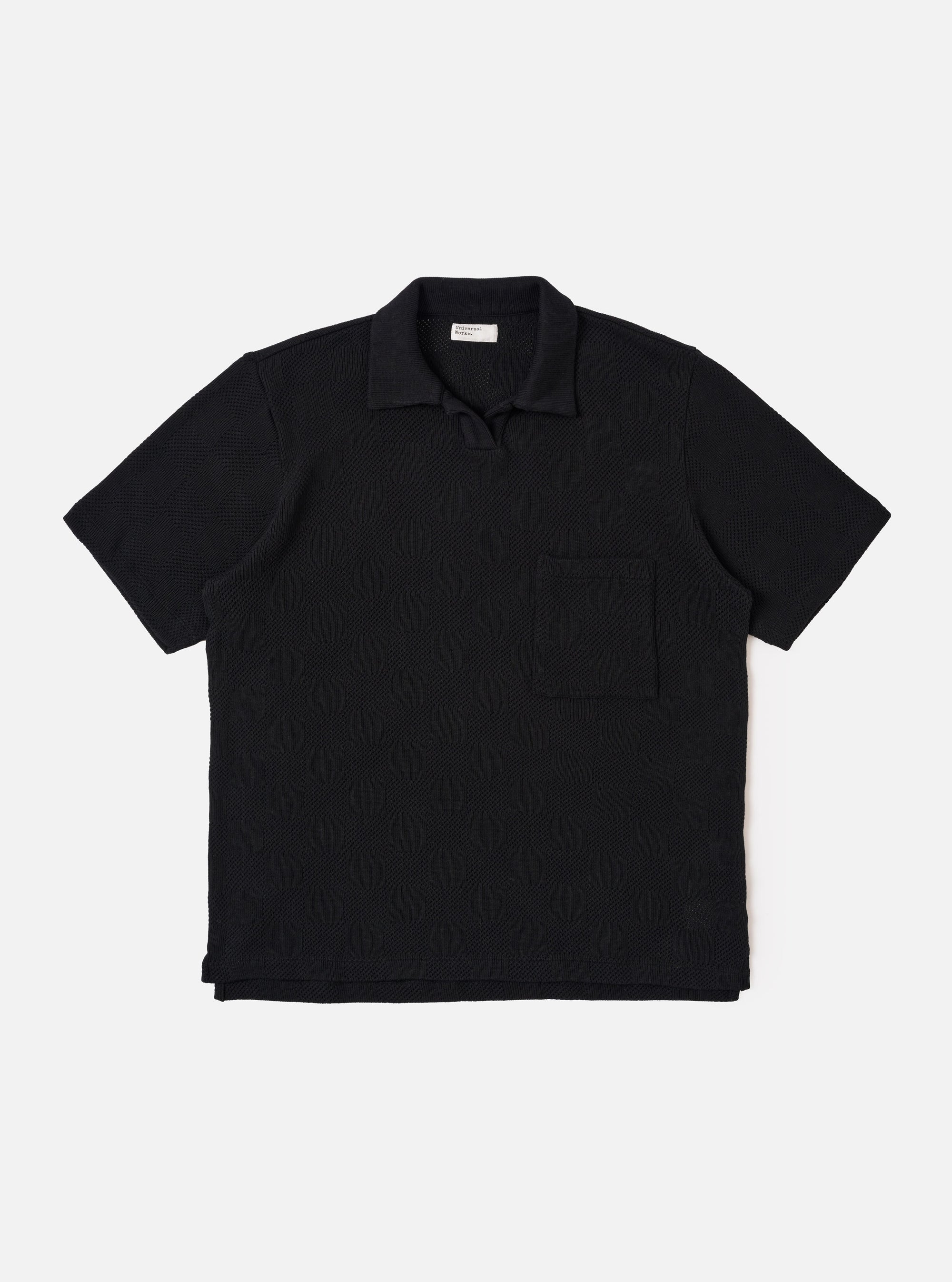 The Black Fantasy Checkerboard Vacation Polo is shown as a flat lay against a white background. The polo features an all-over black and grey checkerboard pattern, a one-piece open collar, a short buttonless placket, and a single patch pocket on the left chest. The short-sleeve garment has a stepped hem with side vents.