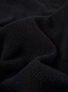 A close-up fabric swatch of the Black Fantasy Checkerboard Vacation Polo highlights the detailed black and grey checkerboard pattern and the texture of the organic cotton material.