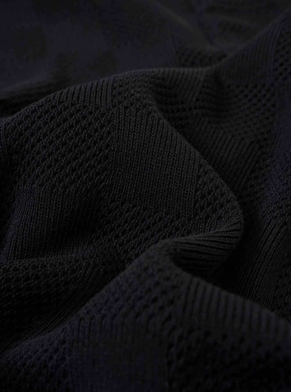 A close-up fabric swatch of the Black Fantasy Checkerboard Vacation Polo highlights the detailed black and grey checkerboard pattern and the texture of the organic cotton material.