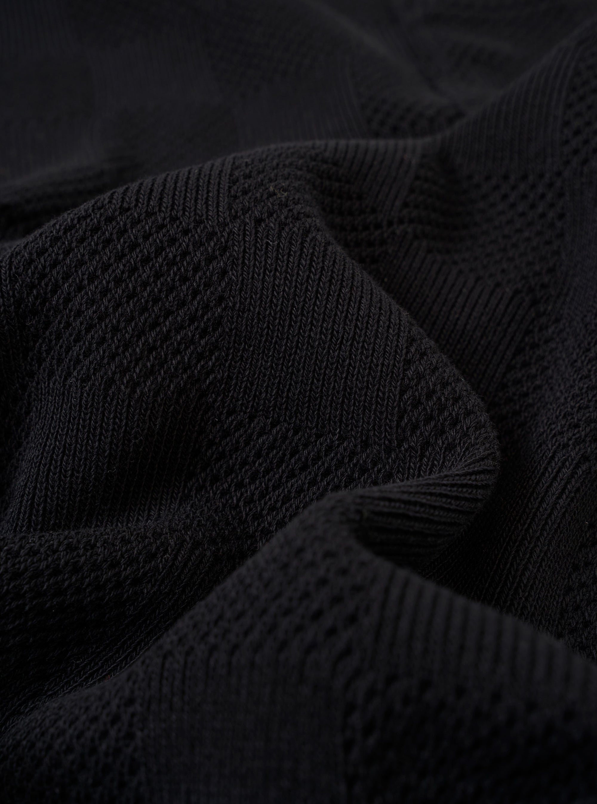 A close-up fabric swatch of the Black Fantasy Checkerboard Vacation Polo highlights the detailed black and grey checkerboard pattern and the texture of the organic cotton material.