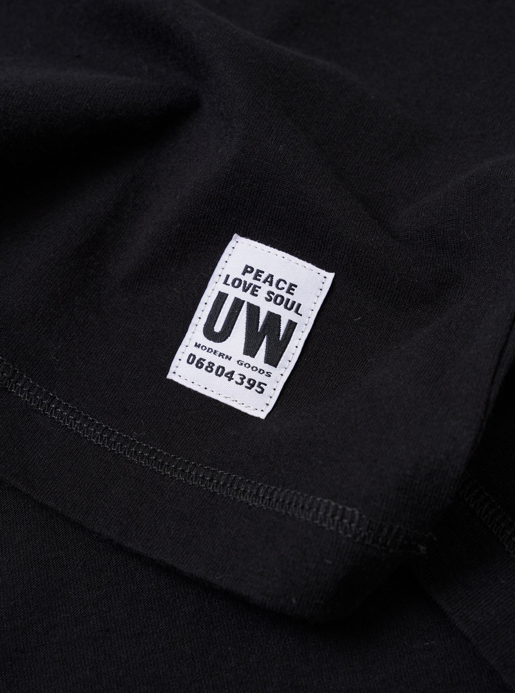 The Black Recycled/Bio Jersey Core Pocket Tee is shown from the back as a flat lay against a plain white background. The image highlights the simple, clean construction of the garment's rear, featuring short sleeves and a straight hem. The fabric is a smooth black jersey made from a blend of recycled and organic cotton.