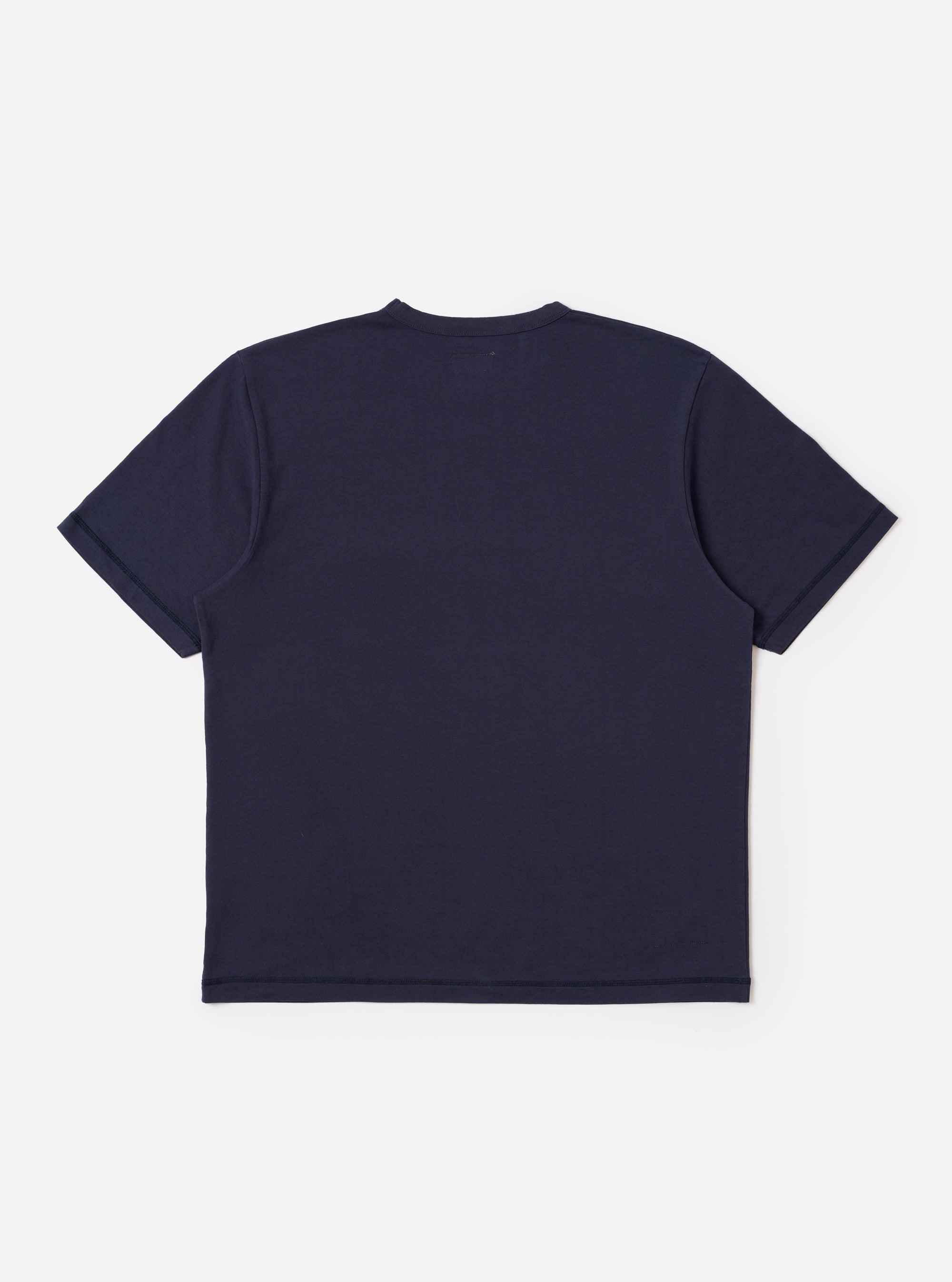 The Navy Recycled/Bio Jersey Core Pocket Tee is shown from the back as a flat lay against a plain white background. The image highlights the shirt's clean construction, straight hem, and the soft texture of the dark navy jersey fabric. A small, subtle brand label is visible at the bottom hem.