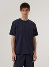 A model wears the Navy Recycled/Bio Jersey Core Pocket Tee against a plain, neutral background. The dark navy short-sleeved t-shirt features a crew neckline and a single patch pocket on the left chest. The image is a medium shot, showing the model from the waist up.
