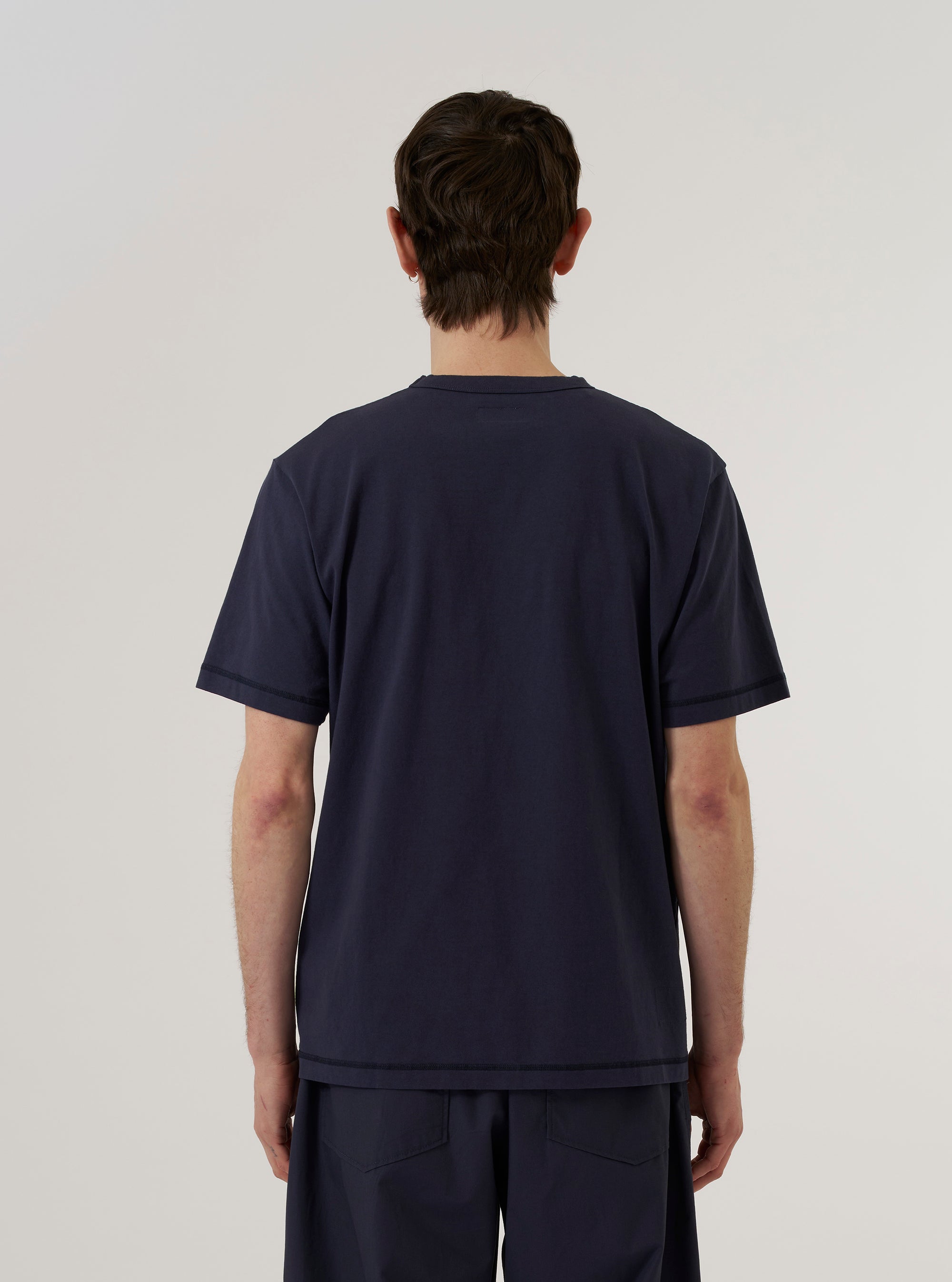 A model wears the Navy Recycled/Bio Jersey Core Pocket Tee, shown from a rear three-quarter angle against a plain white background. The T-shirt features a classic crew neck, short sleeves, and a straight hem. The deep navy blue jersey fabric has a soft, smooth appearance.