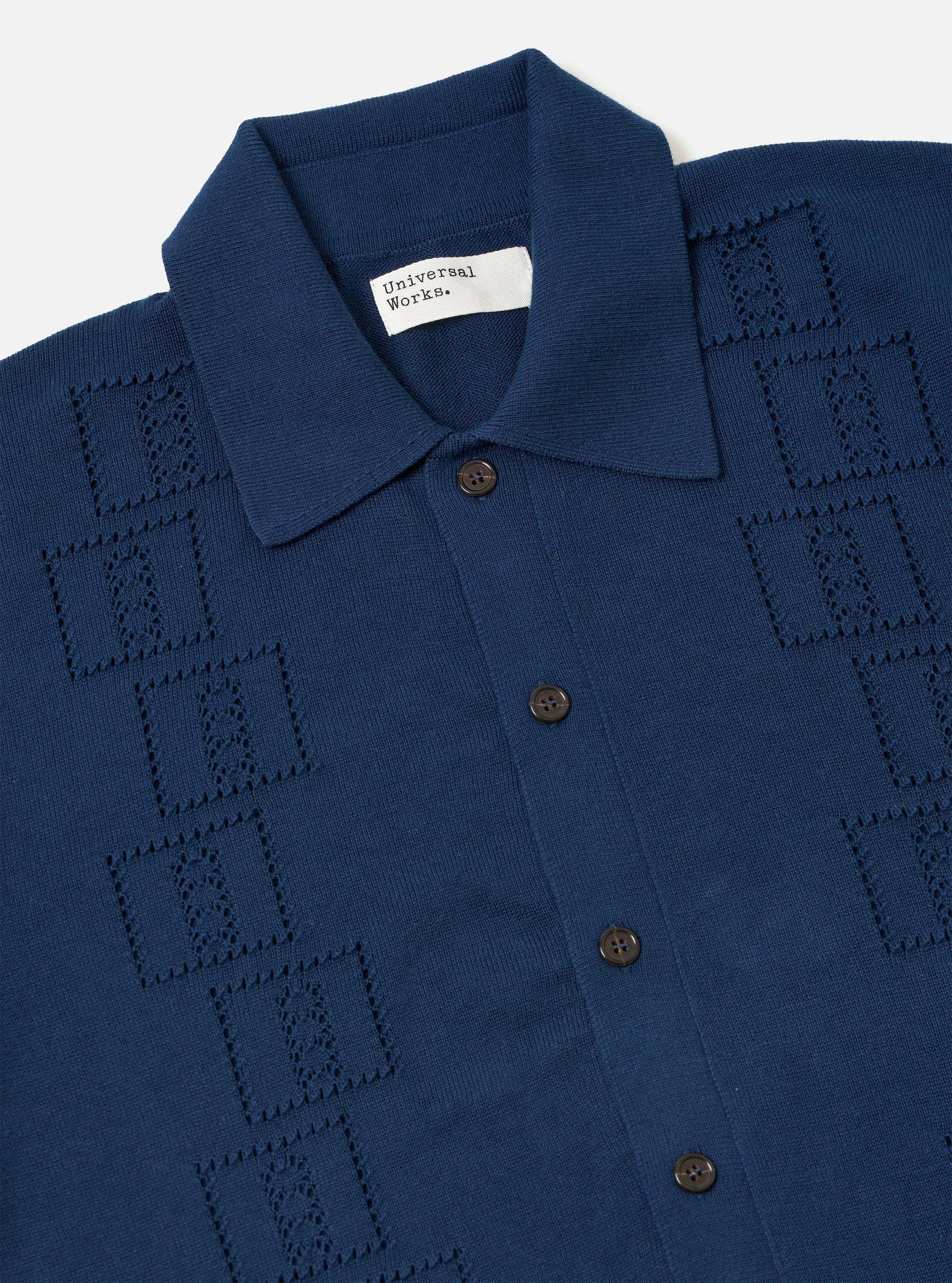 The Dark Navy Cotton Lace Knit Jonny Knit Shirt is shown as a flat lay against a plain white background. The shirt features a short-sleeved, boxy silhouette with a flat split collar and a straight hem. The dark navy cotton fabric is characterized by an intricate, open-textured square lace knit pattern throughout.